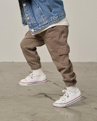 Little Bipsy Cotton Twill Cargo Jogger - Mushroom
Person wearing brown cargo pants, a blue denim jacket, and white sneakers on a gray floor.