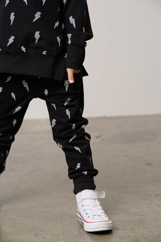 Little Bipsy Lightning Bolt Jogger - Black
Person wearing a black outfit with white patterns and white sneakers on a plain background