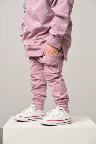 Little Bipsy Smiley Jogger - Dusty Purple
Child wearing a pink outfit with smiley face patterns and white sneakers on a plain background