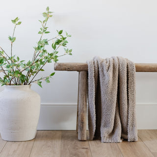 Saranoni Bamboni® Receiving Blanket - Taupe
Gray textured blanket draped over a wooden bench next to a white vase with greenery on a wooden floor.