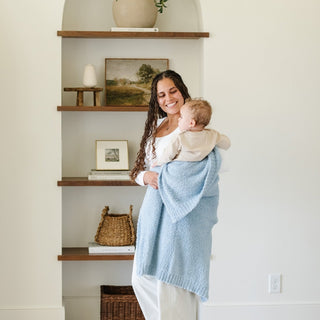 Saranoni Bamboni® Receiving Blanket - Light Blue
Woman holding a baby wrapped in a blue blanket in a home setting with shelves and decor.