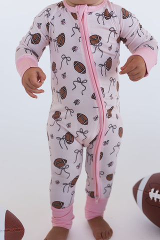 In My Jammers Blush Football Zipper Romper
Baby in a pink and white onesie with football and bow pattern on a white background