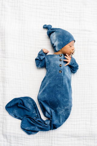 Lou Lou and Company Knotted Gown - Heath
Baby in a blue outfit lying on a white textured surface