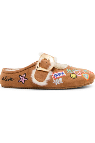 Steve Madden Kid's Faux Fur Nugget - Cognac Multi
A brown suede slip-on mule slipper with a white shearling lining, a gold buckle strap, and colorful embroidered patches on the side, shown against a plain white background.