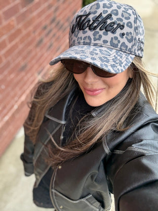 Strong As A Mother® Canvas Hat - Leopard
Woman wearing a leopard print cap with 'Mother' text, sunglasses, and a black jacket.
