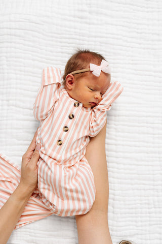 Lou Lou and Company Knotted Gown - Brynn
Newborn baby in a pink and white striped outfit with a bow on a textured white surface