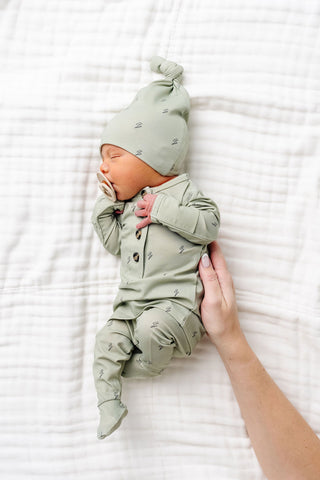 Lou Lou and Company Knit Top and Bottoms - Nash
Newborn baby in a green outfit and hat lying on a white blanket