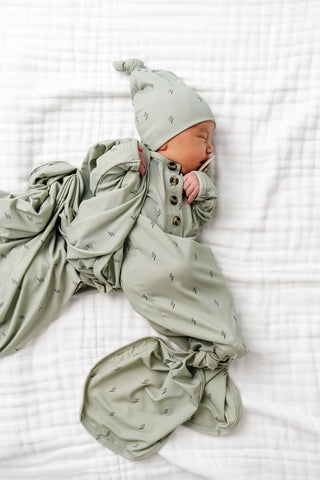 Lou Lou and Company Knit Knotted Gown - Nash
Newborn baby wrapped in a green swaddle with a matching hat on a white textured surface