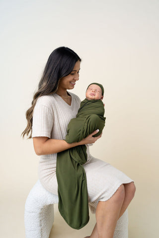 Lou Lou and Company Swaddle Blanket - Riley
Woman holding a baby wrapped in a green blanket against a plain background