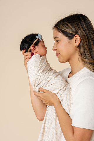 Lou Lou and Company Swaddle Blanket - Kit
Woman holding a baby wrapped in a white blanket against a beige background