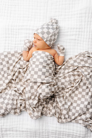Lou Lou and Company Swaddle Blanket - Palmer 
Newborn baby wrapped in a checkered blanket and hat on a white background