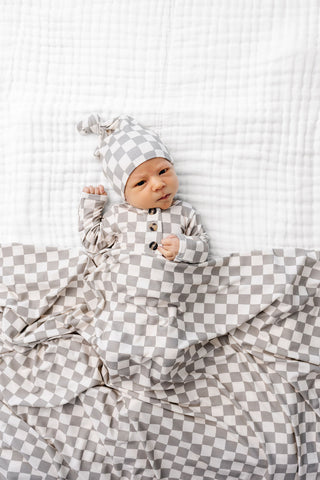 Lou Lou and Company Knotted Gown - Palmer
Newborn baby in a checkered outfit lying on a white textured blanket