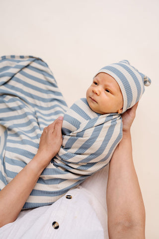 Lou Lou and Company Ribbed Swaddle Blanket - Lincoln
Newborn baby wrapped in a blue and white striped swaddle with a matching hat, held by a person against a plain background.