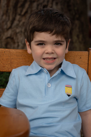 City Beautiful Pencil Polo
Young boy wearing a light blue polo shirt with a logo, sitting outdoors.