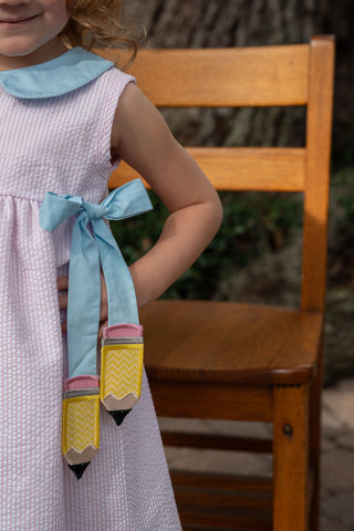City Beautiful Pencil Dress
Child wearing a dress with a pencil-shaped bow tie, sitting on a wooden chair.
