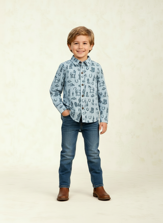 Alto Modas George Shirt- Blue Western Toile 
A young boy stands against a light beige textured studio backdrop, wearing a light blue long-sleeve button-up shirt with a dark blue horseshoe and nail pattern, paired with dark blue jeans and brown boots.