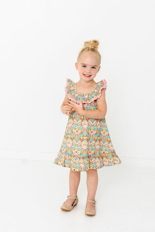 Alto Modas Girls Harper Dress - Happy Sun
Young girl wearing a floral dress holding a toy on a white background