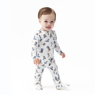 Angel Dear 2 Way Zipper Footie - Buckaroo Boots 
A smiling baby wearing a white footed long-sleeve sleeper with a blue and brown cowboy boot print, standing against a solid white background.