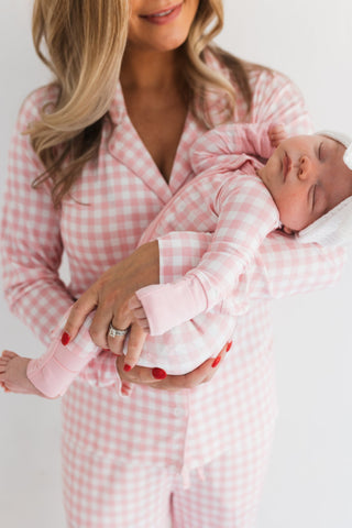 In My Jammers Blush Gingham Zipper Romper
Woman in pink gingham pajamas holding a baby also in pink gingham pajamas.