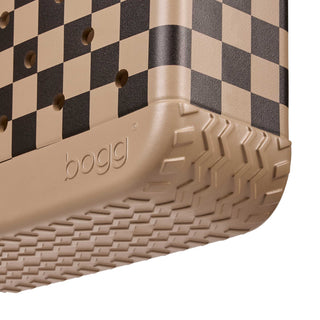 Baby Bogg Bag - Checkered: Camel / Hot Cocoa
Close-up of a Bogg shoe corner showing a beige and black checkerboard pattern on the upper, a tan textured rubber sole, and the embossed Bogg logo on a white background.