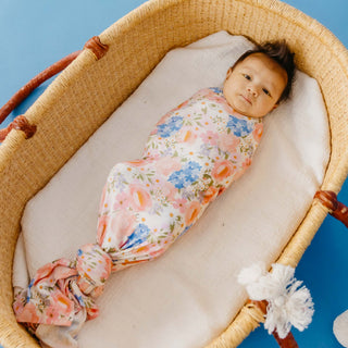 Copper Pearl Bamboo Swaddle Blanket - Penelope
A baby swaddled in a floral-patterned blanket with pink, blue, and orange flowers on a white background, lying inside a woven Moses basket on a blue background.
