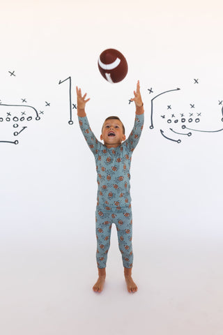 In My Jammers Green Football Two Piece Set
Child in pajamas reaching for a football against a white background with football diagrams.