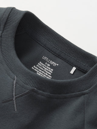 Little Bipsy Pocket Pullover - Shadow
Close-up of a dark gray sweatshirt with 'Little Bipsy' label on a light gray background
