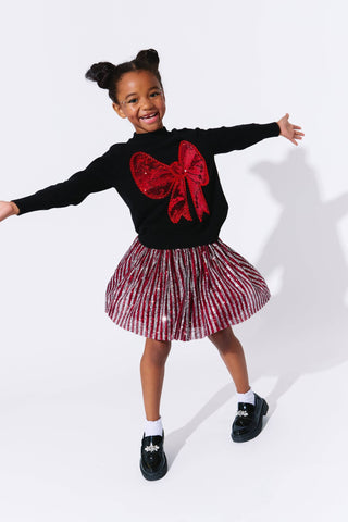 Lola and The Boys Big Bow Sweater
Child wearing a black sweater with a red bow and a red and white striped skirt on a white background