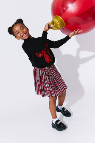 Lola and The Boys Big Bow Sweater
Child holding a large red balloon and a gold trophy on a white background