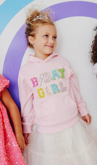Lola and The Boys Birthday Girl Hoodie
Young girl wearing a pink hoodie with 'BIRTHDAY GIRL' text, standing against a colorful circular background.
