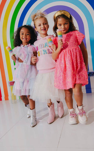 Lola and The Boys Birthday Girl Hoodie
Three young girls in colorful outfits standing in front of a rainbow arch.
