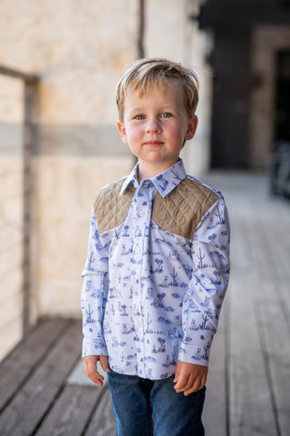 BlueQuail Clothing Co Long Sleeve Shirt - Terlingua Ranch
A young boy wearing a long-sleeve button-down shirt with a blue and white nautical pattern and tan quilted yoke panels, paired with blue jeans, standing on a wooden deck.
