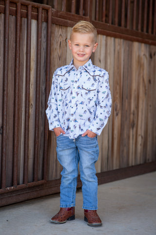 BlueQuail Clothing Co Pearl Snap Long Sleeve Shirt - Rodeo
A young boy stands in front of a rustic wooden fence wearing a white long-sleeve western shirt with a blue floral print, blue jeans, and brown cowboy boots.