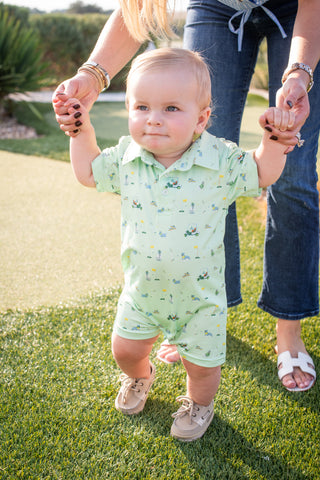 BlueQuail Clothing Co Polo Short Sleeve Romper - Dogwood
Baby in a green romper being held by two adults on grass