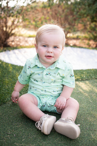 BlueQuail Clothing Co Polo Short Sleeve Romper - Dogwood
Baby sitting on grass wearing a light green outfit with floral patterns.