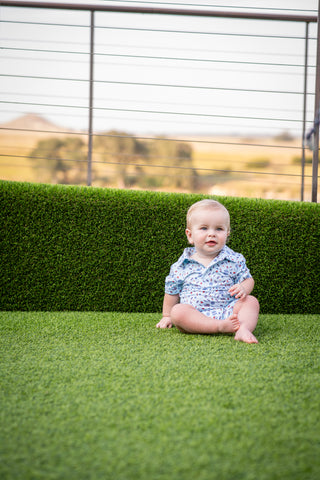 BlueQuail Clothing Co Polo Short Sleeve Romper - Stars & Stripes
Baby sitting on artificial grass with a blurred natural background