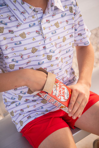 BlueQuail Clothing Co Polo Short Sleeve Shirt - 7th Inning Stretch
Person wearing a patterned shirt and red shorts holding a Cracker Jack box.