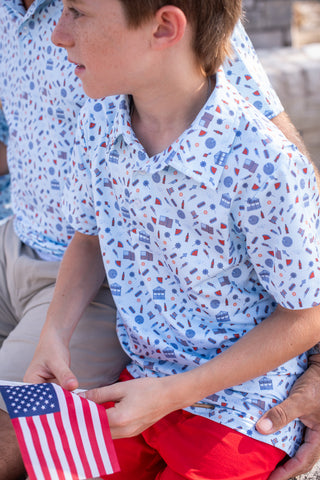 BlueQuail Clothing Co Polo Short Sleeve Shirt - Stars & Stripes
Child holding a small American flag wearing a patterned shirt with a person partially visible behind.