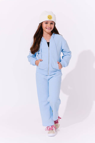 Lola and The Boys Blue Taylor Crystal Set
Child wearing a light blue tracksuit with a white beanie featuring a smiley face on a white background