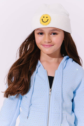 Lola and The Boys Blue Taylor Crystal Set
Young girl wearing a light blue jacket and white beanie with a smiley face emblem on a white background