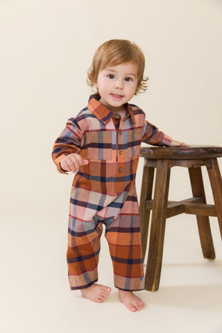 Blue Rooster Baby Boys Easton Jumper - Hayride Plaid
A toddler standing barefoot next to a wooden stool, wearing a long-sleeve plaid button-up shirt and matching pants in rust orange, navy, beige, and white.