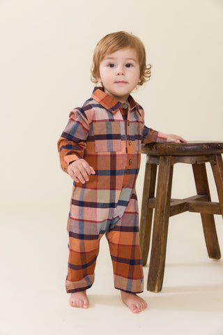Blue Rooster Baby Boys Easton Jumper - Hayride Plaid
A toddler stands barefoot next to a rustic wooden stool, wearing a long-sleeve plaid romper in rust orange, navy blue, and beige tones against a solid cream background.