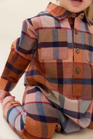 Blue Rooster Baby Boys Easton Jumper - Hayride Plaid
A close-up of a child wearing a long-sleeve plaid button-up shirt and matching plaid pants in warm orange, pink, navy, and beige tones.