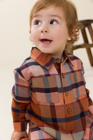 Blue Rooster Baby Boys Easton Jumper - Hayride Plaid
A toddler with light brown hair wearing a long-sleeve plaid button-up shirt in rust orange, navy blue, and beige tones, looking up and smiling.