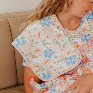Copper Pearl Burp Cloth Set - Penelope
A close-up lifestyle shot of a woman wearing a floral print maternity nursing top and holding a baby. The top features a soft pink border and a delicate pattern of blue, pink, and orange flowers on a white background.
