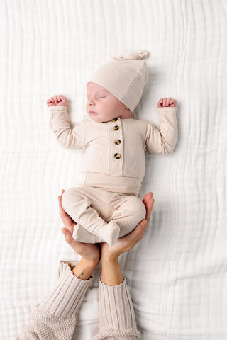 Lou Lou and Company Ribbed Top and Bottoms - Cove
Newborn baby in a cream outfit being held on a white textured surface