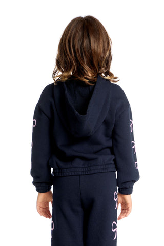 Chaser Semi Cropped Shirred Stormy Bows Hoodie Pullover
Child wearing a navy tracksuit with white text on sleeves against a white background