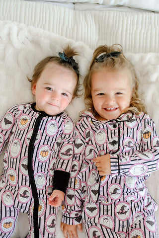 Caden Lane Girl's Two Piece Flare Lounge Set - Glow in the Dark Galloween
Two young children lying side by side on a white blanket, wearing matching Halloween-themed long-sleeve pajamas with pink and black stripes and witch motifs.