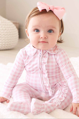 Caden Lane Peter Pan Collar Ruffle Zipper Footie - Rosy Gingham
Baby wearing a pink checkered outfit with a large bow on a neutral background