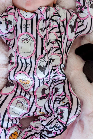 Caden Lane Ruffle Zipper Footie - Glow in the Dark Galloween
A close-up of a baby's torso wearing a Halloween-themed footed sleeper. The sleeper has a white base with black vertical stripes, pink scalloped borders, and cartoon ghost, bat, spider, and pumpkin motifs.